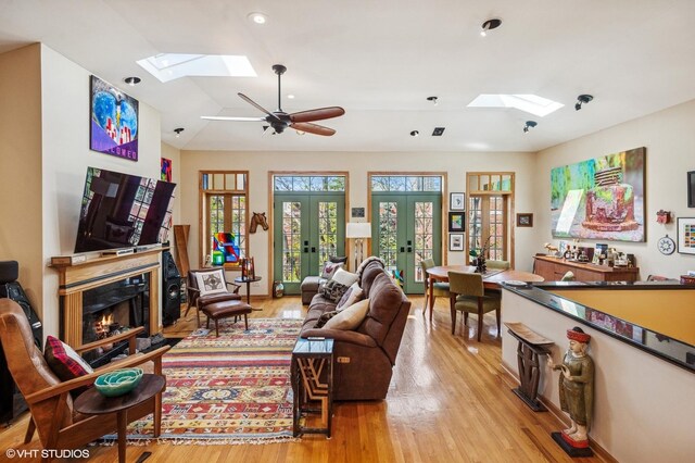 dining space featuring a skylight, light wood finished floors, a ceiling fan, lofted ceiling, and a glass covered fireplace