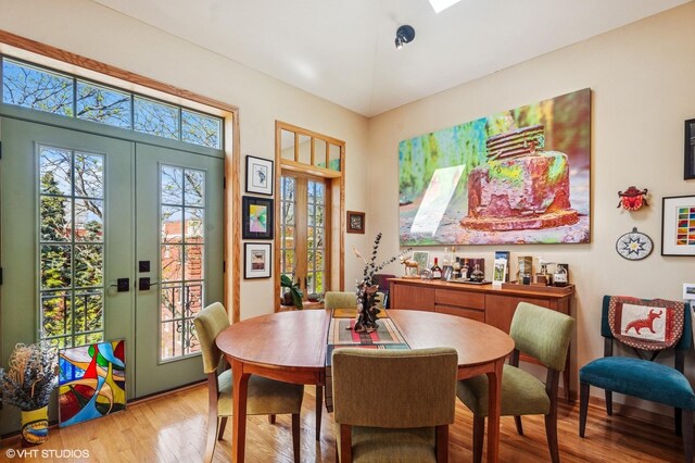 living room with a skylight, light wood-style floors, french doors, a warm lit fireplace, and recessed lighting