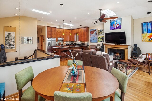 living room featuring ceiling fan, wood finished floors, a lit fireplace, a skylight, and vaulted ceiling