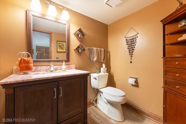 half bathroom with toilet, wood finished floors, vanity, and baseboards