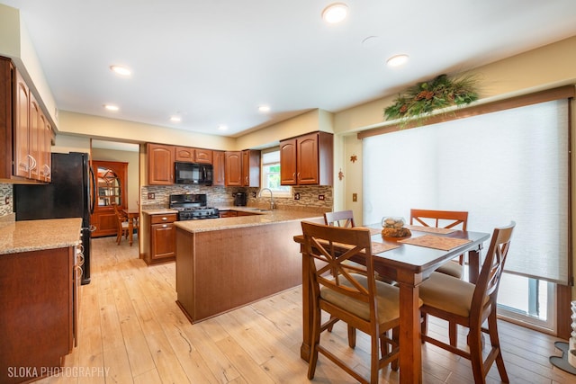 kitchen featuring black appliances, a sink, backsplash, light wood-style floors, and brown cabinetry