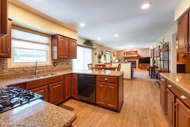 kitchen featuring a sink, black dishwasher, a glass covered fireplace, backsplash, and a peninsula