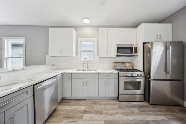 kitchen featuring appliances with stainless steel finishes, a sink, light stone counters, and light wood-style flooring