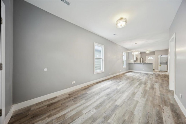 unfurnished living room with light wood-type flooring and baseboards