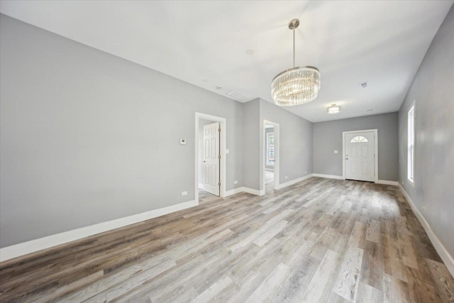 empty room featuring a chandelier, light wood-style floors, and baseboards