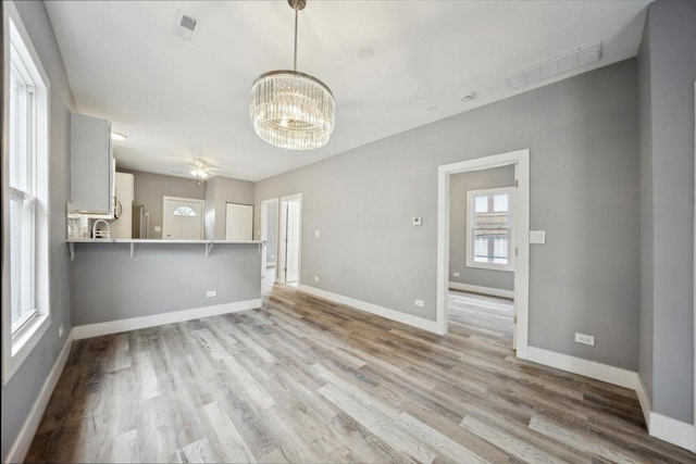 unfurnished living room with baseboards, light wood finished floors, a chandelier, and a sink