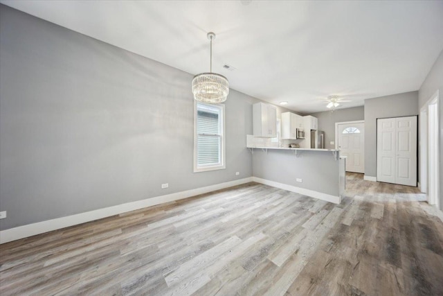 unfurnished living room with plenty of natural light, a chandelier, baseboards, and light wood-style floors