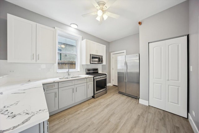 kitchen featuring appliances with stainless steel finishes, a sink, light wood-style floors, light stone counters, and ceiling fan