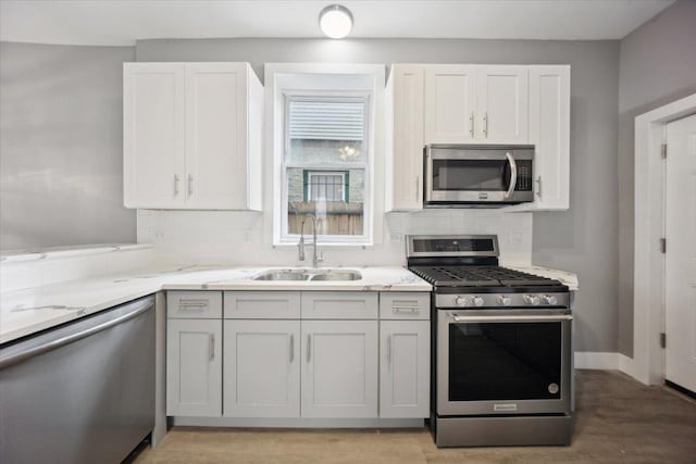 kitchen featuring stainless steel appliances, a sink, decorative backsplash, light stone counters, and light wood-style flooring