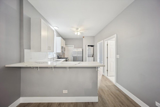 kitchen featuring stainless steel appliances, light wood-style flooring, baseboards, a ceiling fan, and a sink