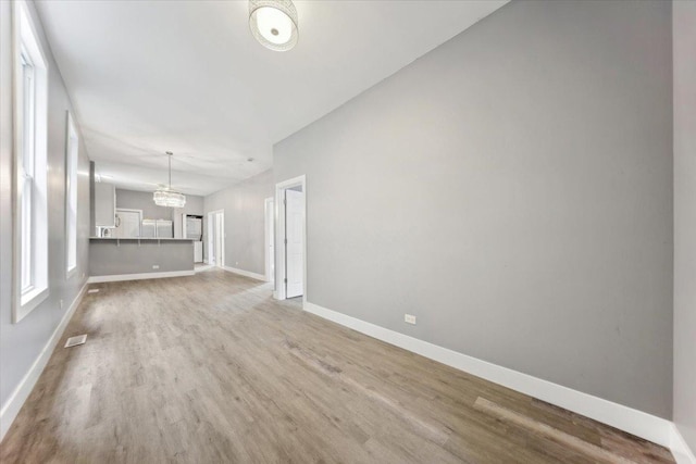 unfurnished living room with baseboards, a chandelier, and wood finished floors