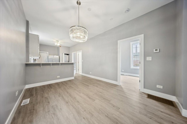 unfurnished living room featuring a chandelier, light wood finished floors, baseboards, and ceiling fan
