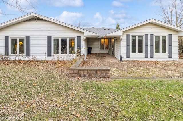rear view of house with roof with shingles and a lawn