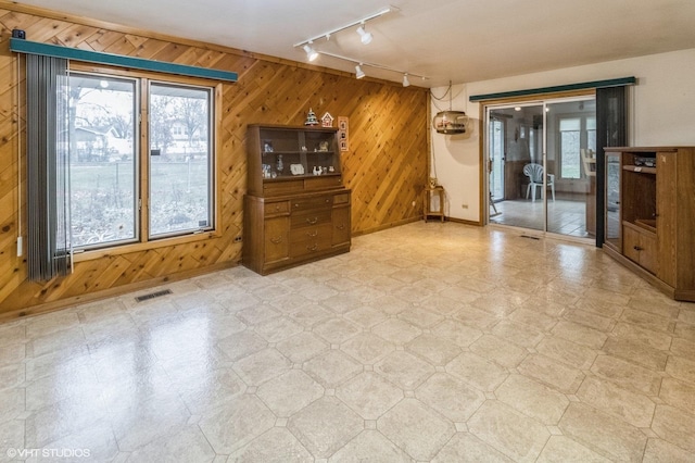 unfurnished living room with rail lighting, tile patterned floors, wood walls, and baseboards
