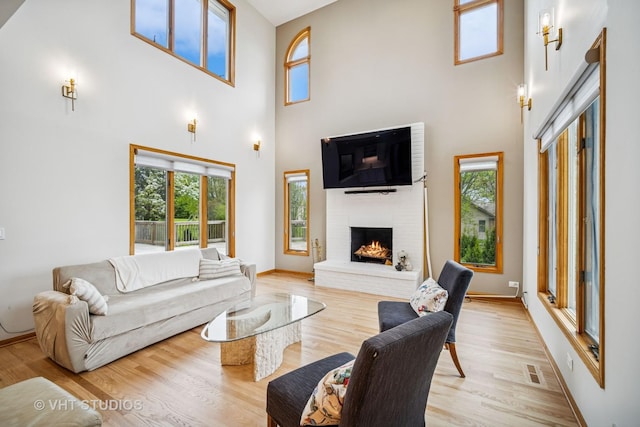 living room featuring a towering ceiling, healthy amount of natural light, a fireplace, light wood-style flooring, and baseboards
