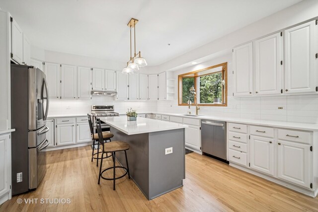 kitchen with appliances with stainless steel finishes, under cabinet range hood, decorative backsplash, and light wood-style floors