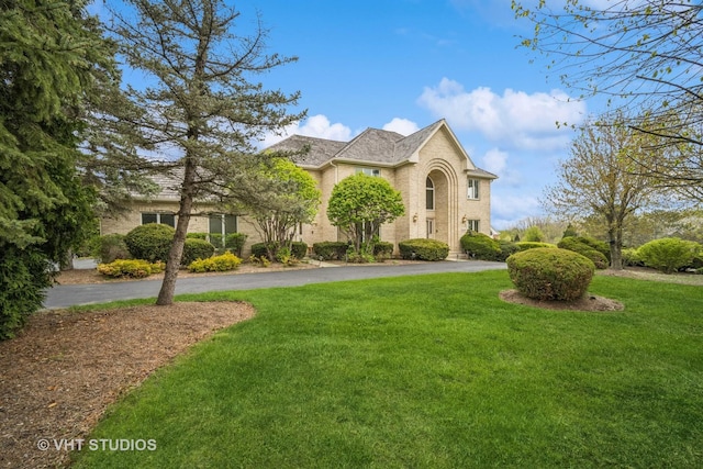traditional home with a front yard, asphalt driveway, and brick siding