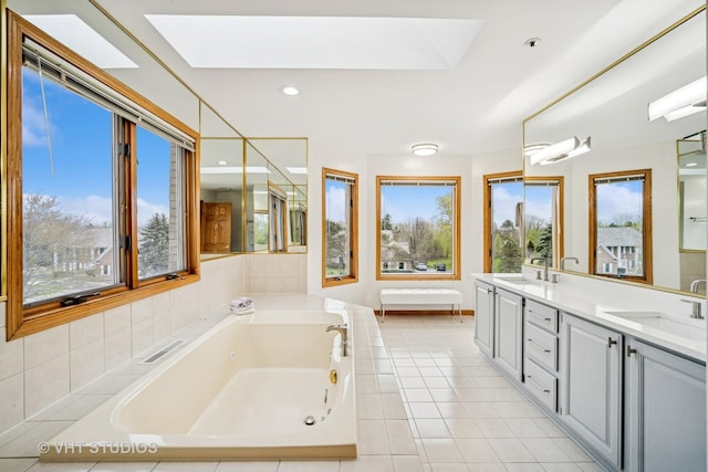 bathroom with a skylight, a jetted tub, double vanity, and tile patterned flooring