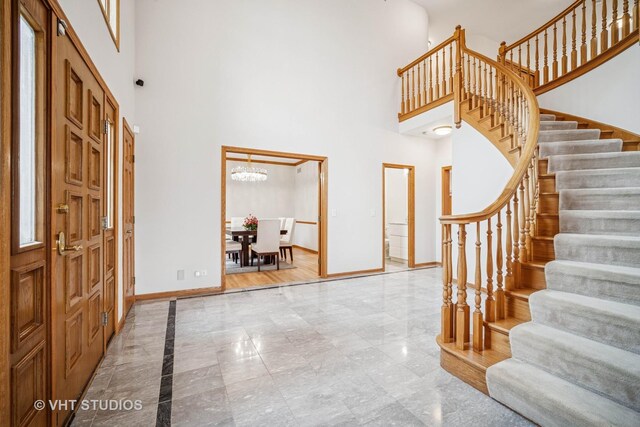 foyer with a towering ceiling, baseboards, stairway, a chandelier, and marble finish flooring