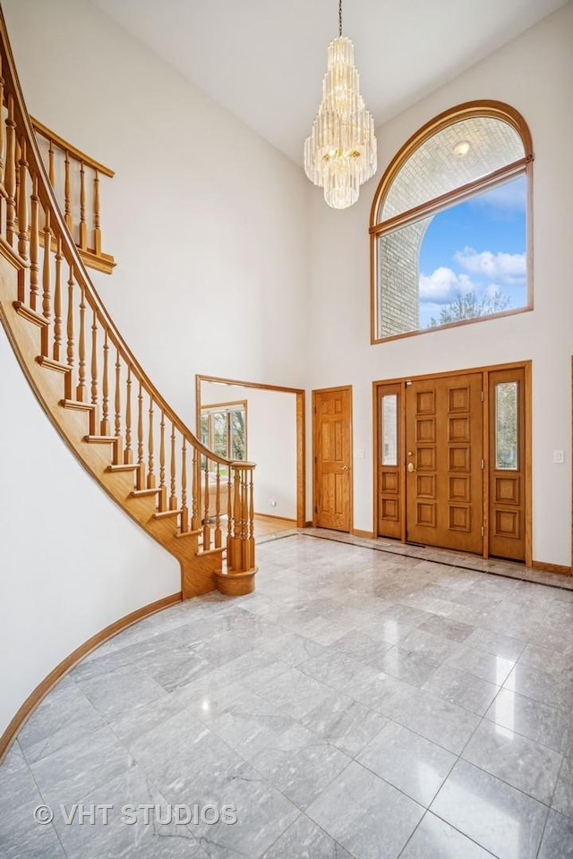 foyer entrance with a towering ceiling, marble tiled floors, baseboards, a chandelier, and stairs