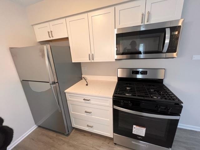kitchen with stainless steel appliances, white cabinets, baseboards, and wood finished floors
