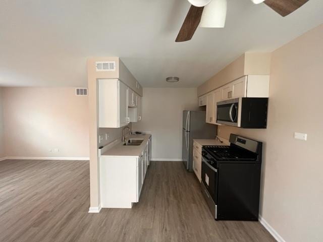 kitchen with stainless steel appliances, ceiling fan, a sink, and wood finished floors