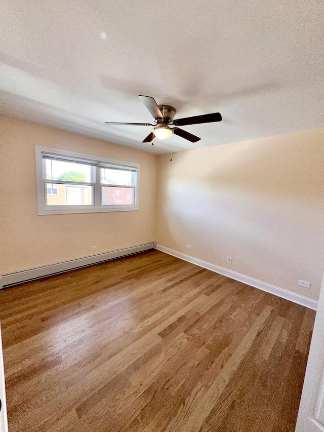 spare room with baseboard heating, wood finished floors, baseboards, and a ceiling fan