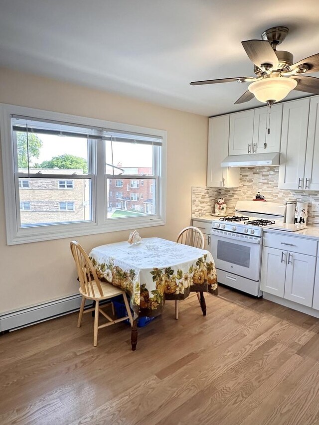 kitchen with white gas range, under cabinet range hood, light wood-style flooring, and plenty of natural light
