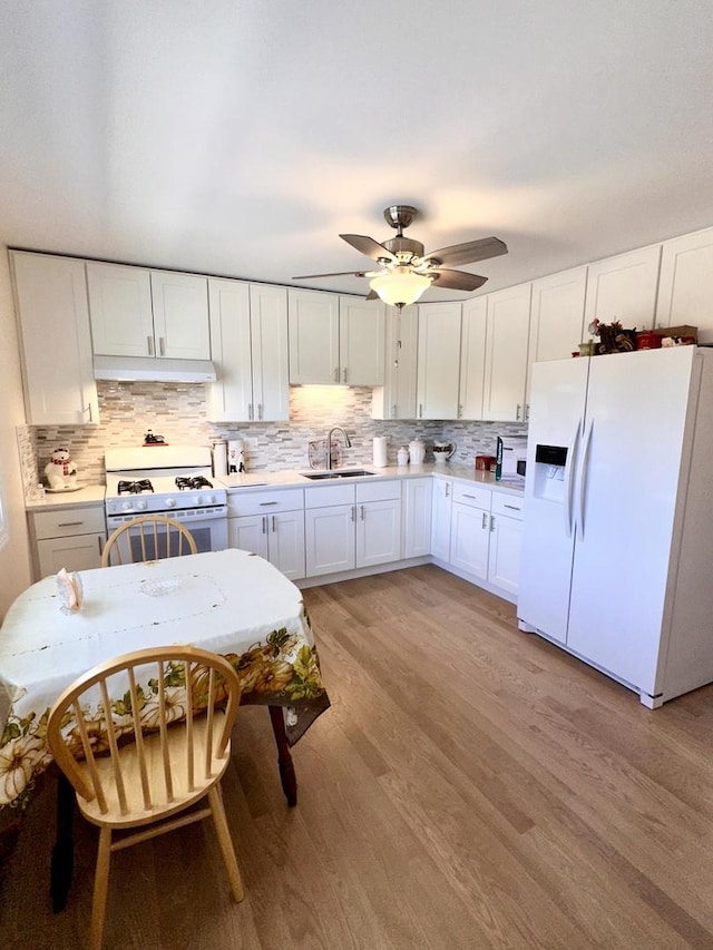kitchen with white appliances, under cabinet range hood, a sink, light wood finished floors, and white cabinets