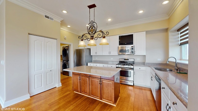 kitchen featuring appliances with stainless steel finishes, stacked washer / dryer, a sink, decorative light fixtures, and a kitchen island
