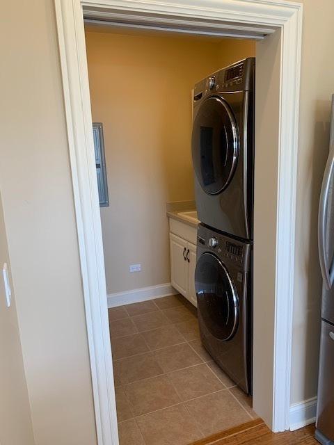 laundry area featuring stacked washer / drying machine, cabinet space, light tile patterned flooring, and baseboards