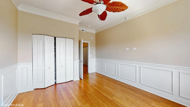 unfurnished bedroom with a closet, light wood-style floors, ornamental molding, a wainscoted wall, and ceiling fan