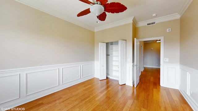 unfurnished bedroom with ornamental molding, light wood finished floors, a closet, wainscoting, and a decorative wall