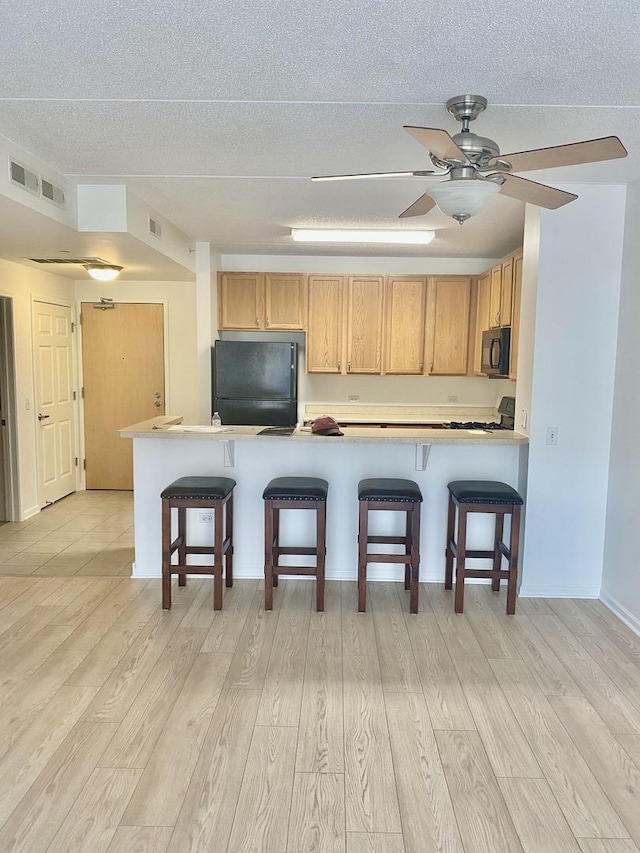 656 Pearson St Unit 608C, Des Plaines, IL 60016 - kitchen with black appliances, a breakfast bar area, light wood-type flooring, light countertops, and a textured ceiling