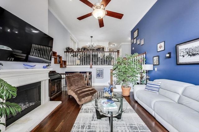 living area featuring ornamental molding, wood finished floors, a ceiling fan, a chandelier, and a fireplace with raised hearth