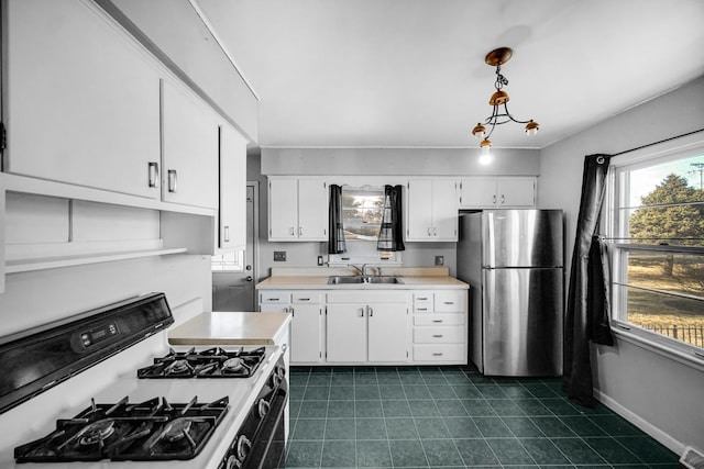 kitchen with gas stove, freestanding refrigerator, a sink, light countertops, and white cabinets