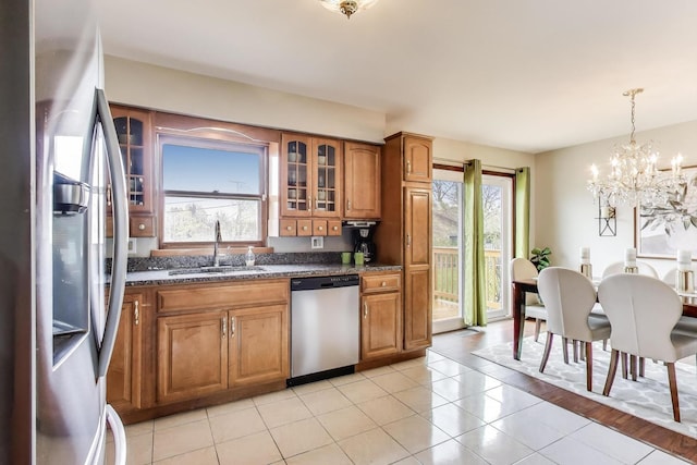 kitchen featuring appliances with stainless steel finishes, a sink, brown cabinetry, a chandelier, and glass insert cabinets
