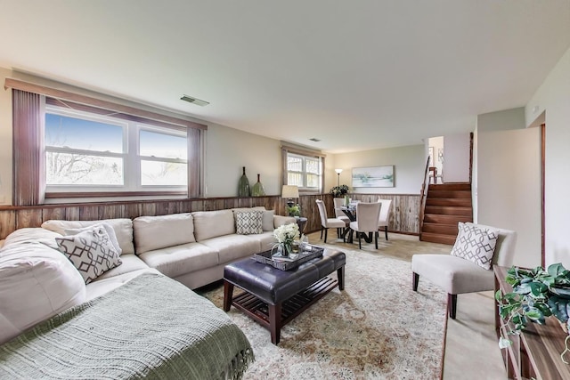 living room with stairs, wooden walls, and a wainscoted wall