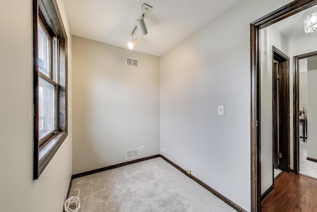 empty room featuring baseboards, rail lighting, and carpet