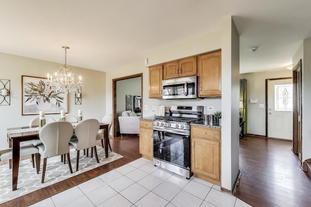 kitchen with stainless steel appliances, a chandelier, wood finished floors, dark stone counters, and pendant lighting
