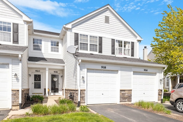 multi unit property featuring stone siding, a garage, driveway, and roof with shingles