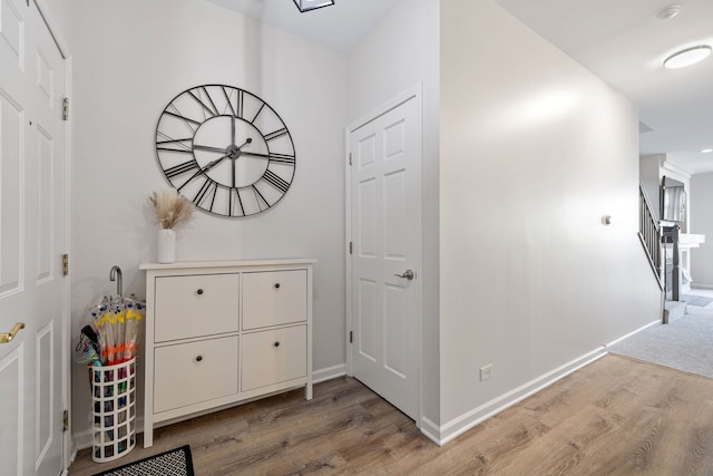 hall with light wood-type flooring, baseboards, and stairway