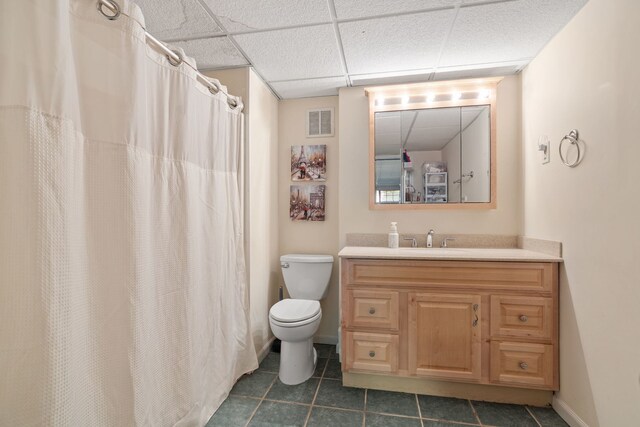 bathroom featuring a drop ceiling, tile patterned flooring, toilet, vanity, and baseboards