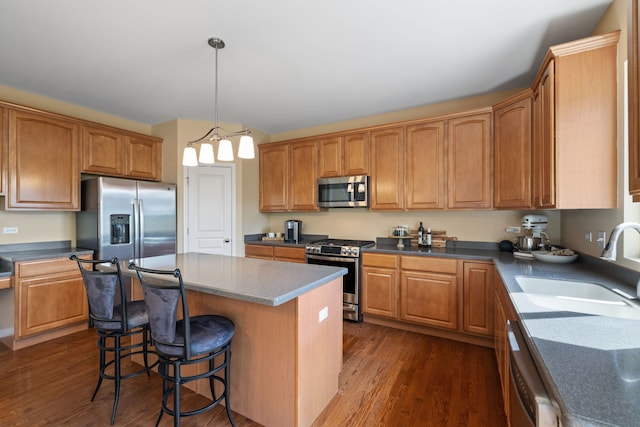kitchen with appliances with stainless steel finishes, dark wood-type flooring, a sink, and a breakfast bar area