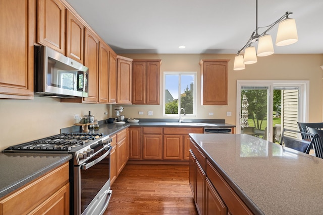 kitchen with stainless steel appliances, a sink, wood finished floors, pendant lighting, and recessed lighting