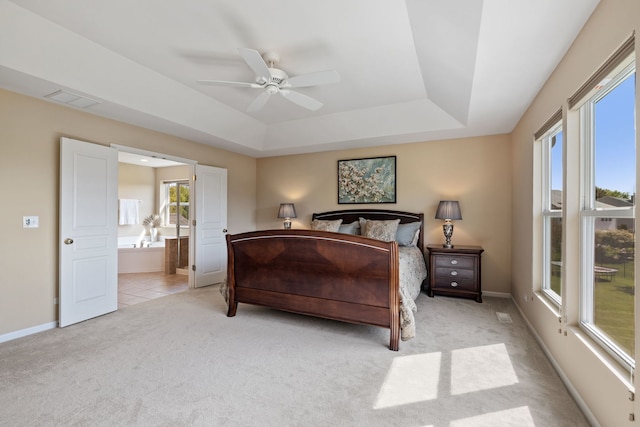 bedroom featuring light carpet, a raised ceiling, connected bathroom, and baseboards