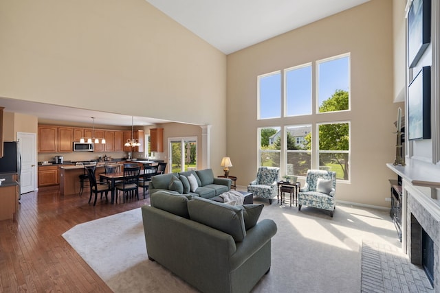 living area featuring a towering ceiling, a fireplace, a chandelier, and dark wood-type flooring