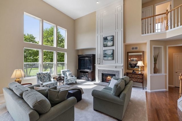living room featuring a towering ceiling, a fireplace, healthy amount of natural light, wood finished floors, and baseboards