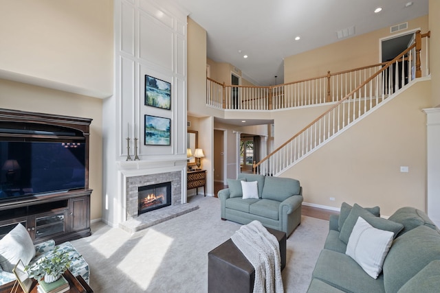 living area featuring stairway, a glass covered fireplace, a high ceiling, baseboards, and recessed lighting
