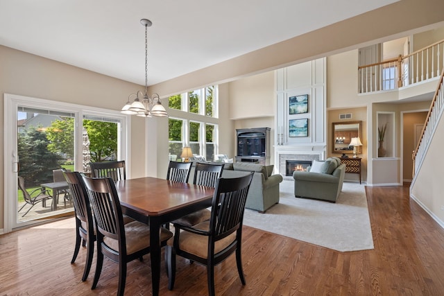 dining room featuring a chandelier, wood finished floors, a glass covered fireplace, baseboards, and a towering ceiling
